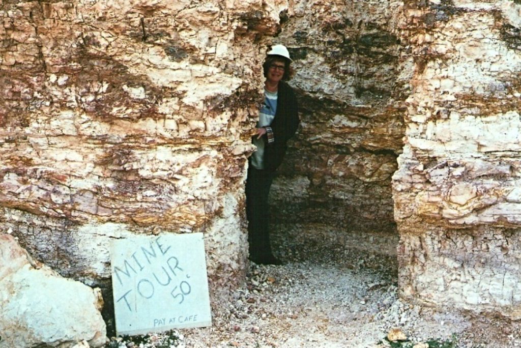 Person standing at the entrance of an opal mine in New South Wales, Australia, ready to lead a tour as advertised on a hand-written sign.