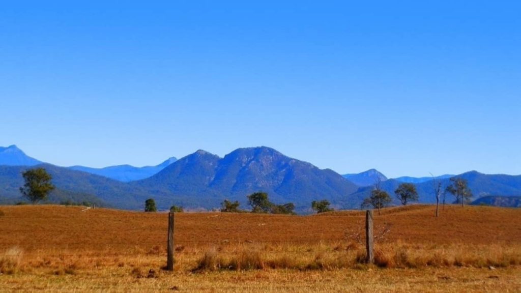 A scenic view of mountain silhouettes in the Scenic Rim, with grassy fields in the foreground.