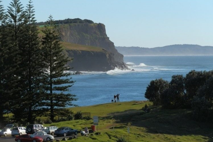 A picturesque view of Skennars Head, with towering cliffs, waves crashing against the shoreline, and visitors enjoying the scenic landscape—one of the breathtaking things to do in Ballina NSW for coastal photography and sightseeing.
