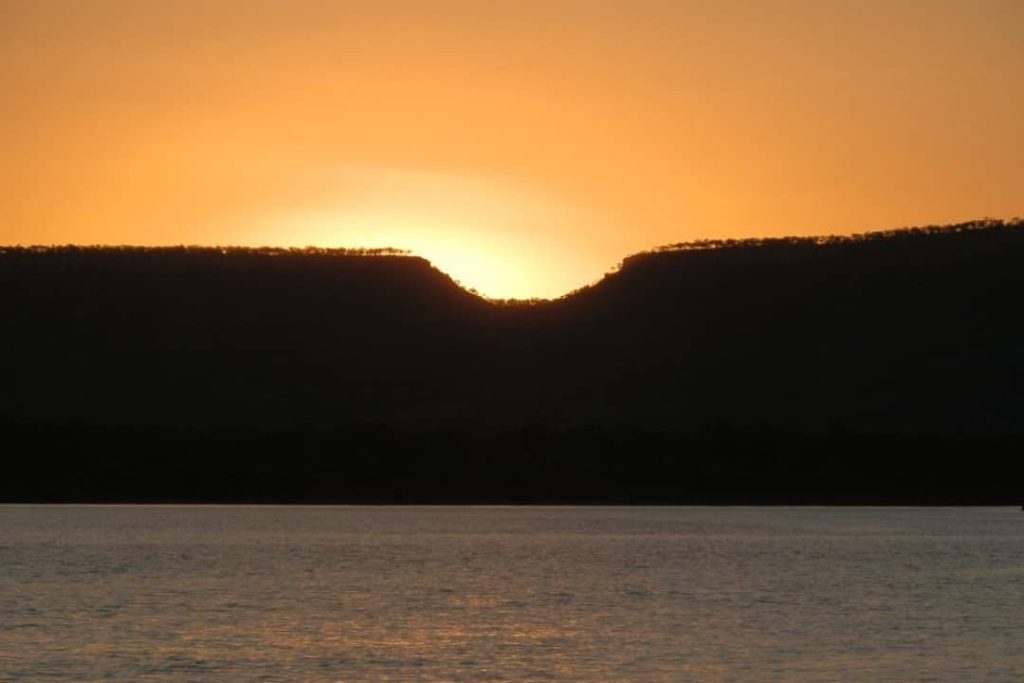 Sunset over the Victoria River, illuminating the horizon in a golden glow as it dips between distant hills near Timber Creek, Northern Territory.