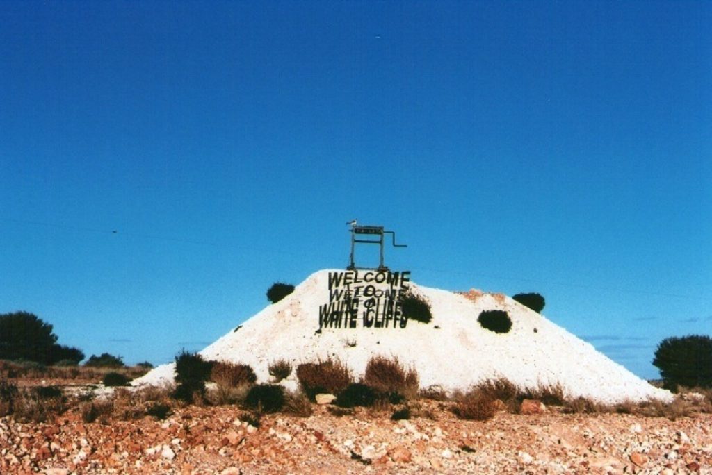 Welcome sign on a mound at the entrance of White Cliffs, New South Wales, featuring an iconic opal mining structure.