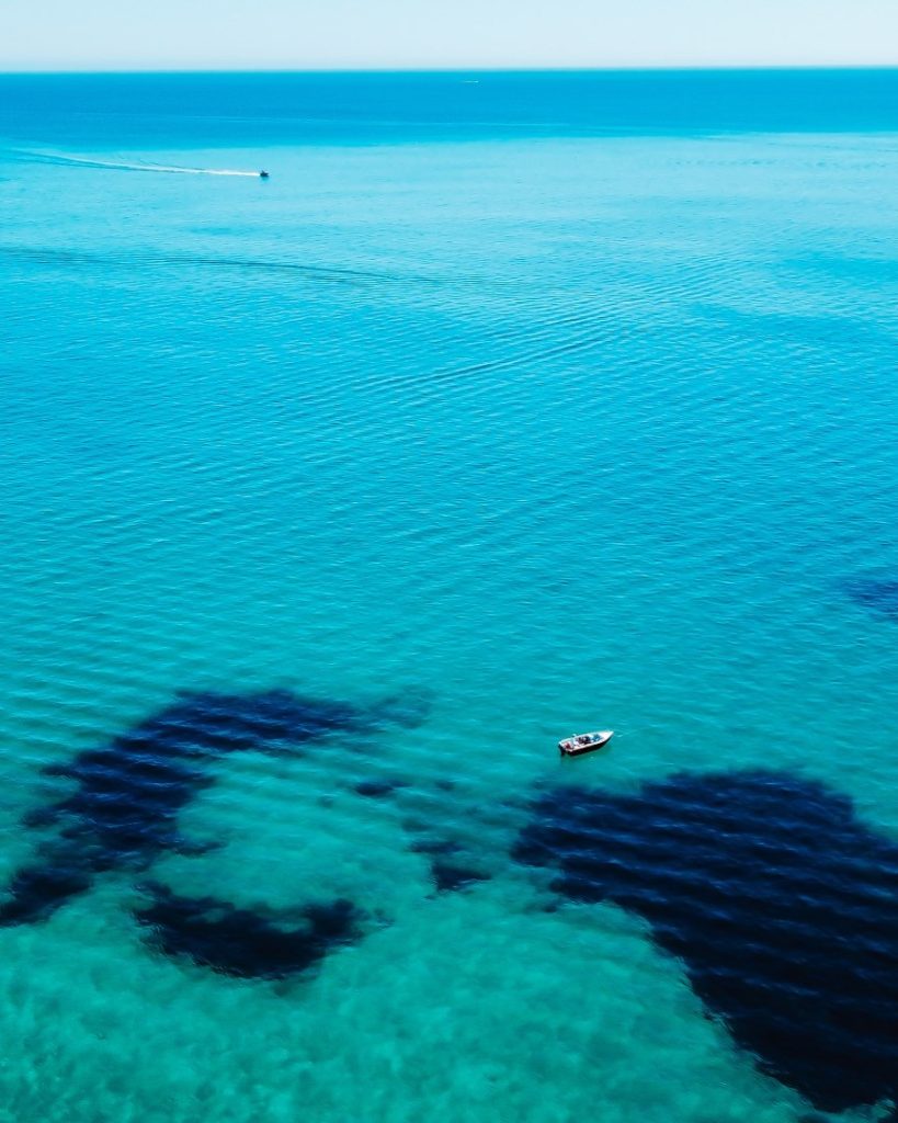 Small boat floating over clear turquoise water with dark patches, near Busselton Jetty, popular for snorkelling.