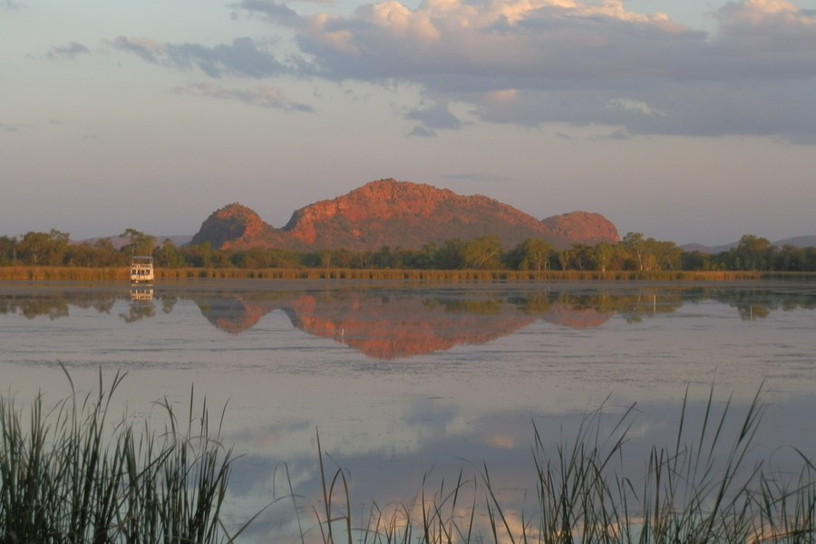 View of the Sleeping Buddha rock formation reflected in the still waters of Lily Creek Lagoon during sunset in Kununurra, Western Australia.