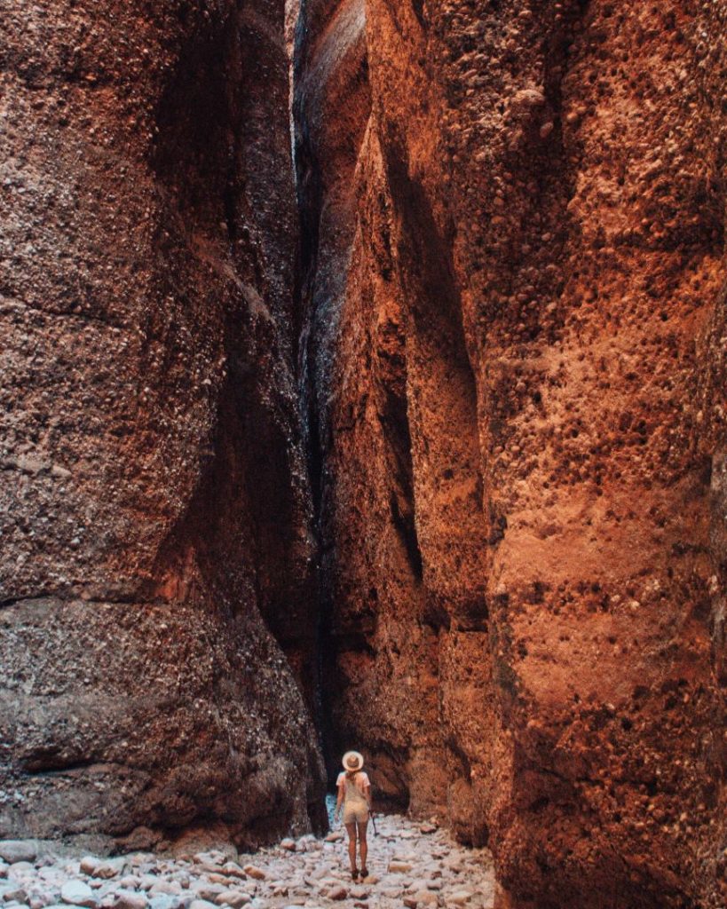 A person standing in the narrow gorge of Cathedral Gorge, surrounded by towering red and orange sandstone walls