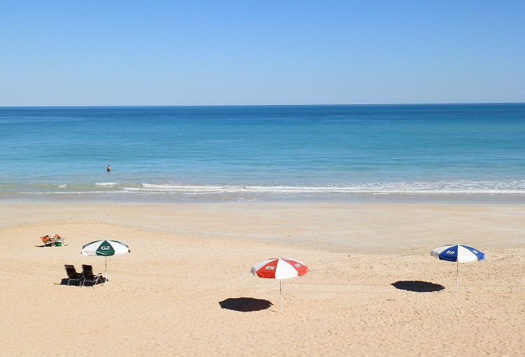 Colorful beach umbrellas and sun loungers on the golden sands of Cable Beach, with turquoise waters and clear skies in the background.