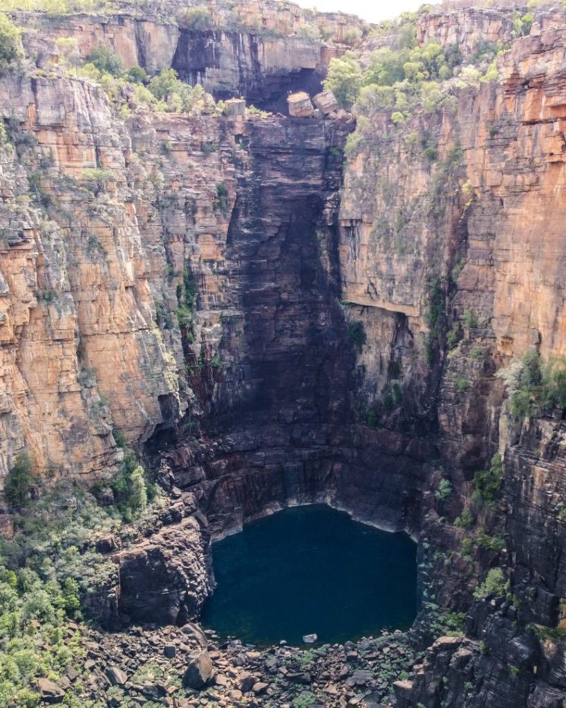 A dramatic vertical rock face of Jim Jim Falls, Kakadu National Park, with a deep pool at the base during the dry season.