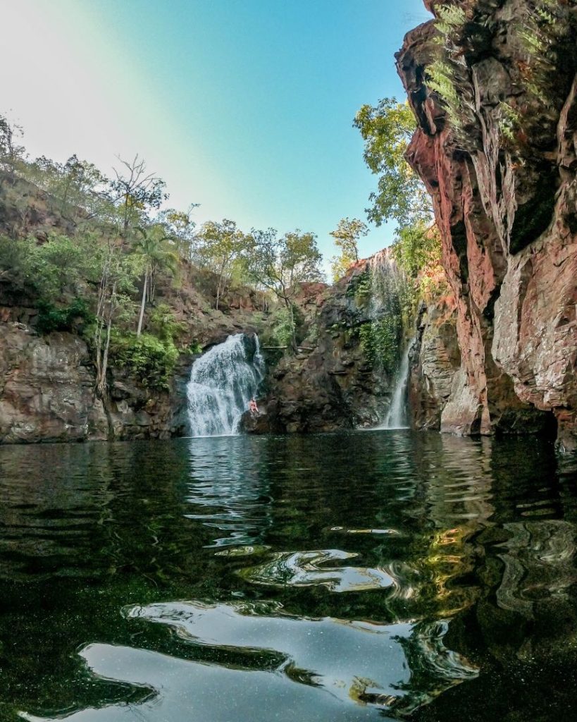A natural waterfall cascading into a still pool, surrounded by cliffs and lush vegetation in Litchfield National Park, Northern Territory