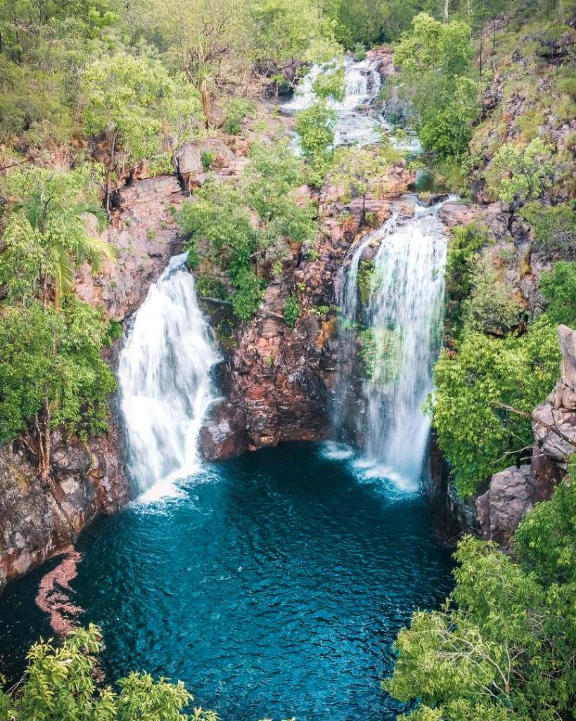 Aerial view of Florence Falls cascading into a deep blue plunge pool surrounded by lush greenery in Litchfield National Park.