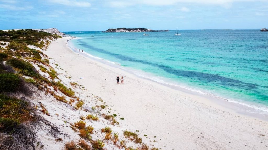 A scenic view of Hamelin Bay, Western Australia, showing white sandy shores, turquoise waters, and a couple walking along the beach.