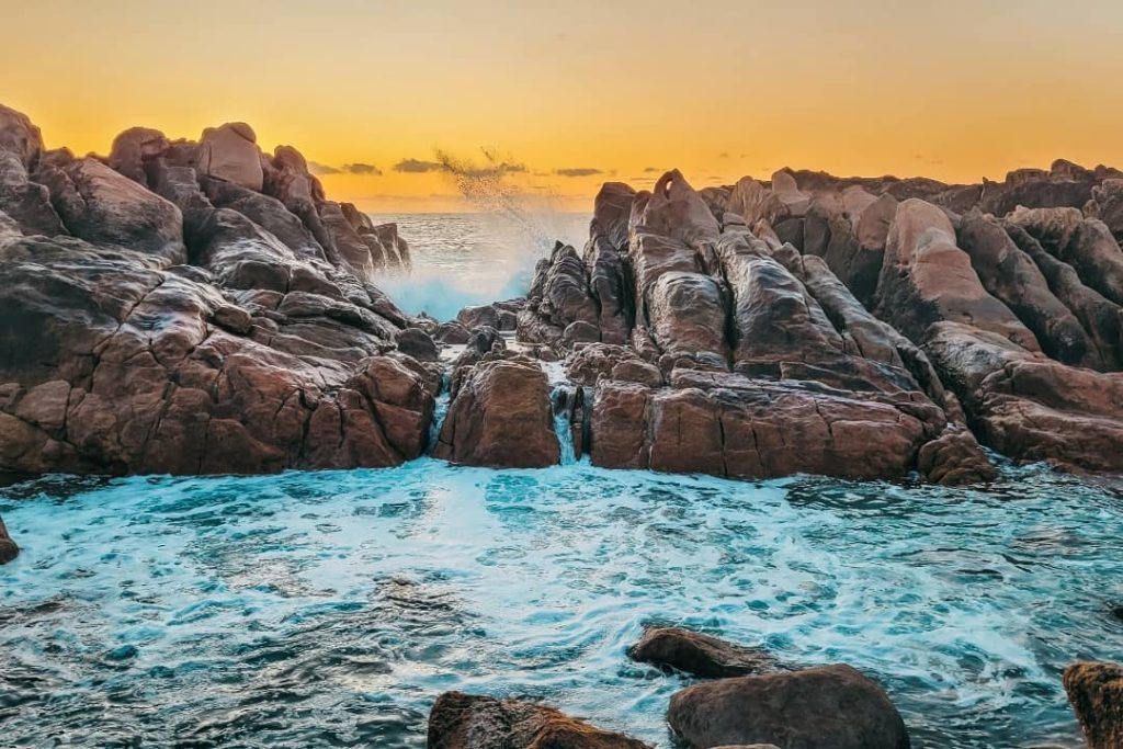 Waves crashing into rugged rocks at Injidup Natural Spa in Yallingup during a golden sunset, creating a dramatic seascape.