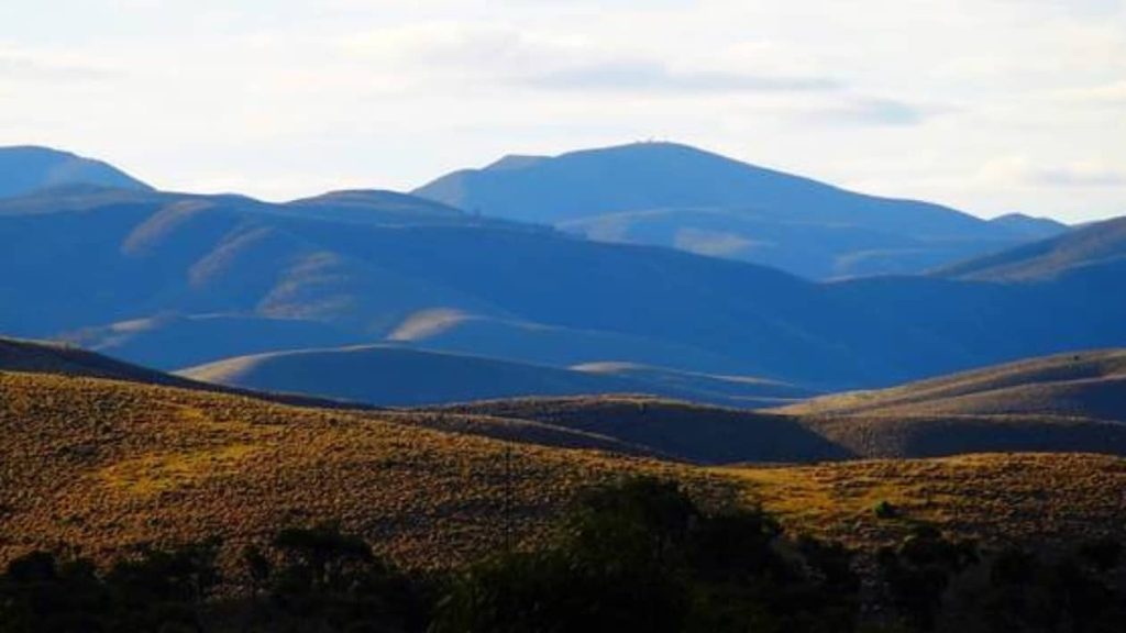 A serene view of rolling hills bathed in late afternoon light, with shadows emphasizing the contours and distant peaks marking the end of the Dutchman’s Stern Summit hike.