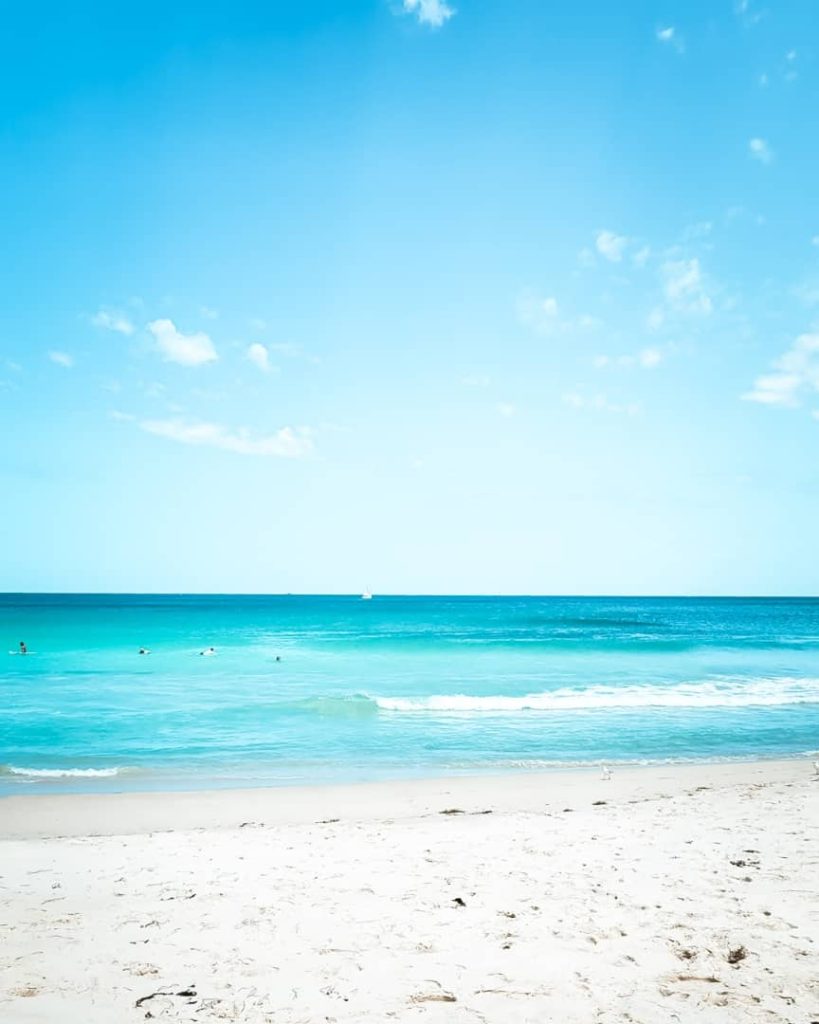 A pristine view of Scarborough Beach in Perth, Western Australia, with clear blue skies, turquoise waters, and gentle waves washing ashore onto white sand.