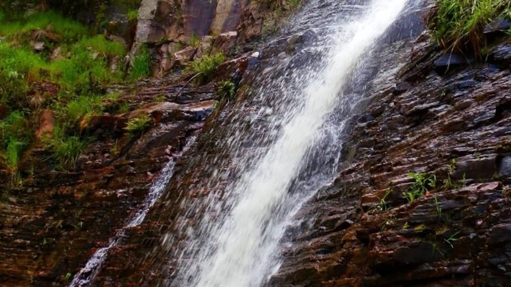 A cascading stream of water flows over mossy, rocky cliffs at Silverband Falls in Victoria, surrounded by greenery.