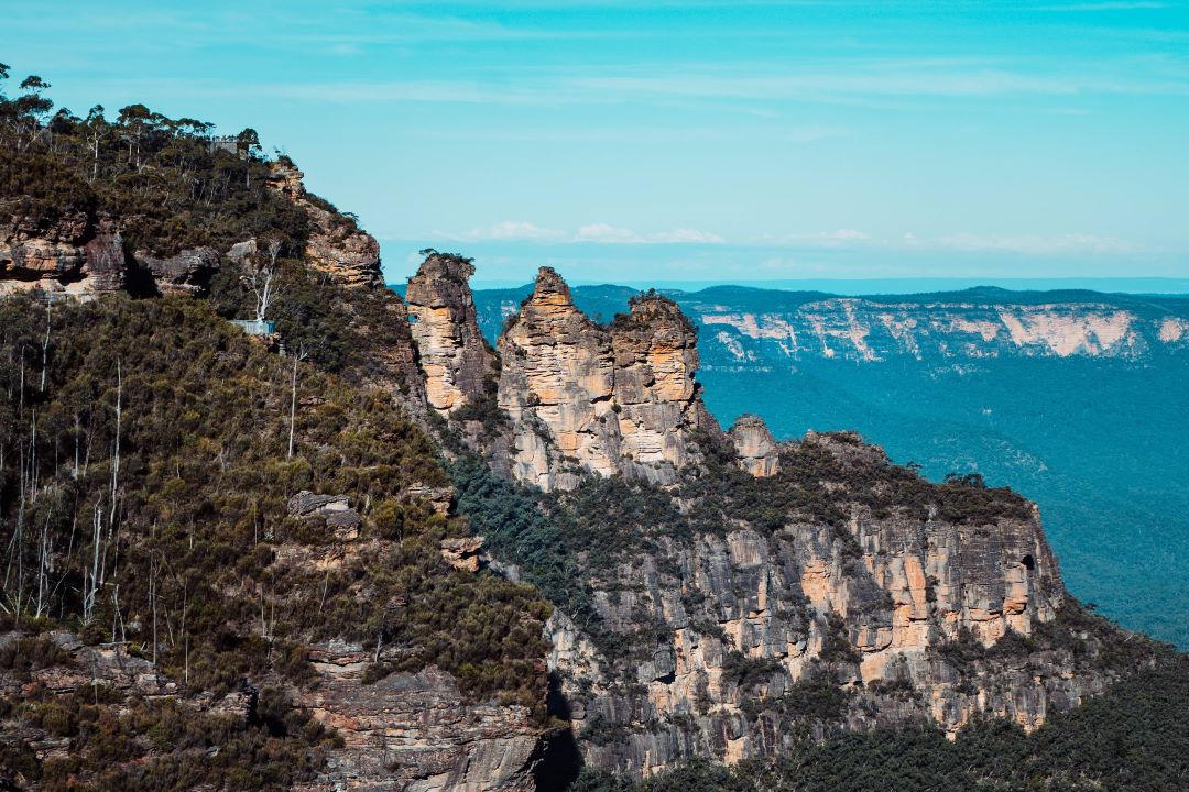Scenic view of the Three Sisters rock formation in the Blue Mountains, Australia, surrounded by lush greenery under a bright blue sky. The best time to visit this iconic location is spring, when the flowers bloom and the weather is mild.