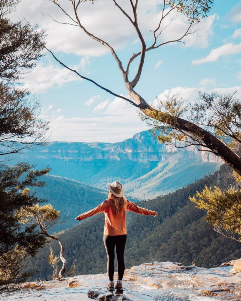 Woman standing at the top of a small cascade in Fortress Falls surrounded by lush greenery, a must-see spot featured in the best tours in the Blue Mountains. A perfect setting for nature lovers.