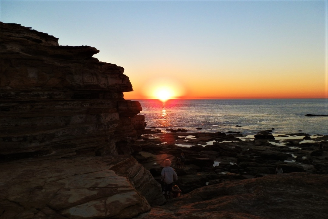 A vibrant sunset at Gantheaume Point, Broome, with golden hues reflecting on the rocky coastline and calm waters. It's one of the best sunsets in australia