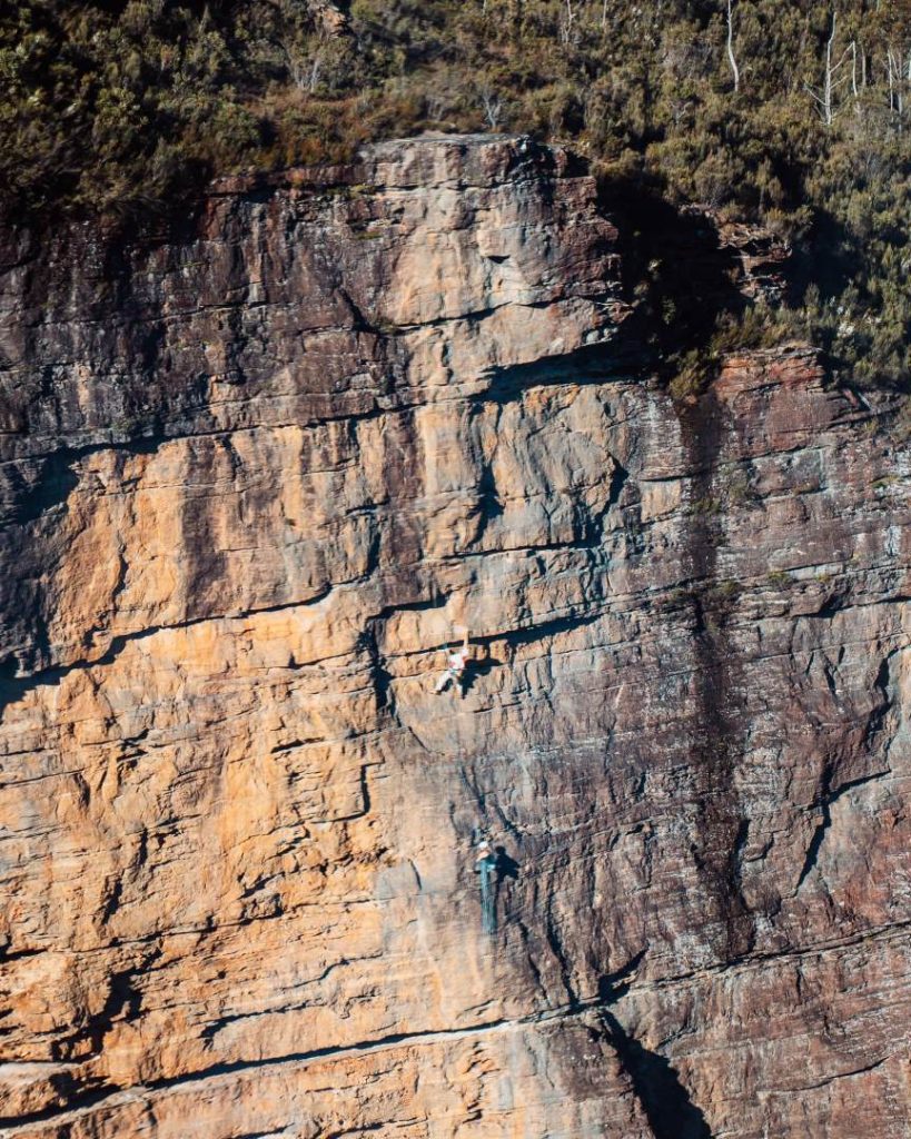 An adventurer abseiling down a rugged cliff in the Blue Mountains, part of an exhilarating and great tour in the Blue Mountains. The steep rock face and lush surroundings amplify the thrill.