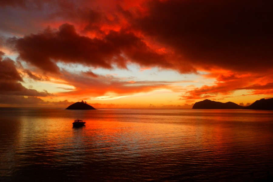A fiery red and orange sunset over the ocean, with Lord Howe Island's distinctive silhouette in the distance.