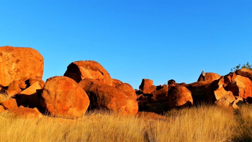 The setting sun casts warm light on the iconic boulders at Devils Marbles in the Northern Territory, Australia.