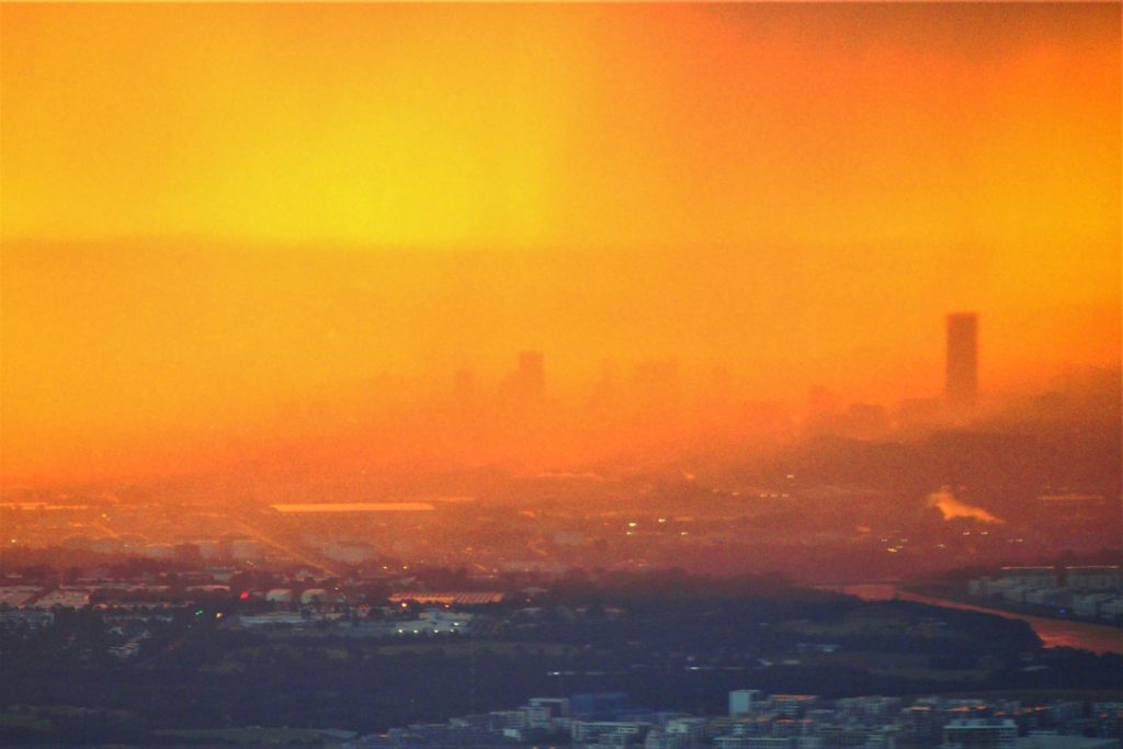 The Sydney skyline, shrouded in smoke haze, glows under a vibrant orange sunset in New South Wales, Australia.