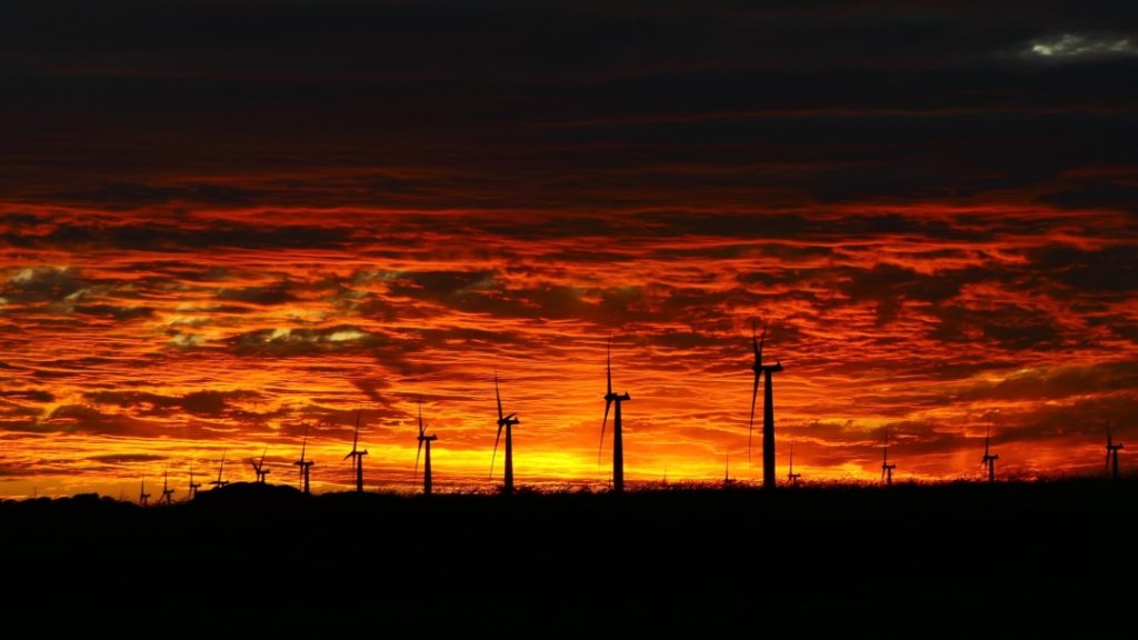 Wind turbines stand silhouetted against a dramatic orange sunset at Wattle Point Wind Farm in Yorke Peninsula, South Australia, Australia.