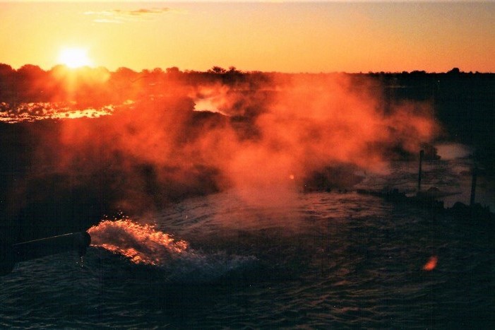 Steam rises from bore water during a vibrant sunset in Thargomindah, Queensland, Australia, casting warm orange light across the scene.