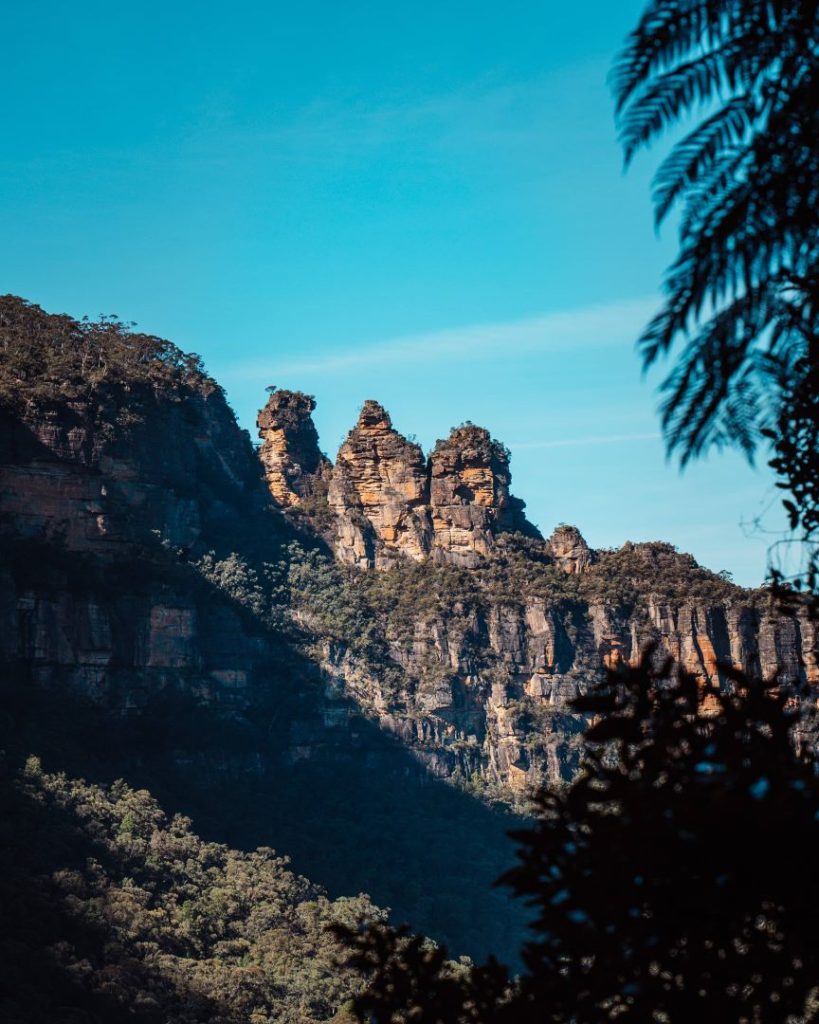 The iconic Three Sisters rock formation in the Blue Mountains, framed by lush greenery and bright blue skies, often featured in the best tours of the Blue Mountains. A symbol of local Aboriginal legend.