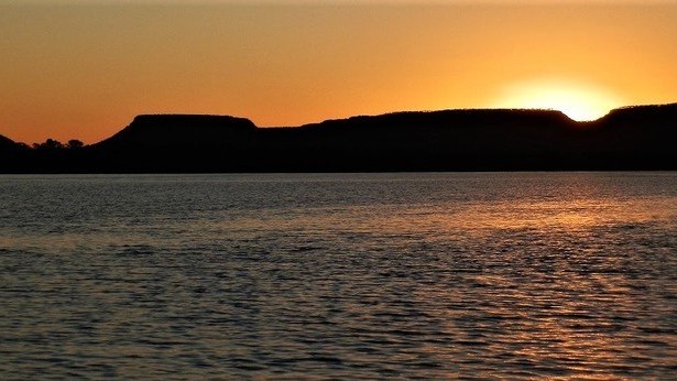 A golden sunset over the Victoria River in Timber Creek, Northern Territory, Australia, with rocky escarpments silhouetted in the distance.