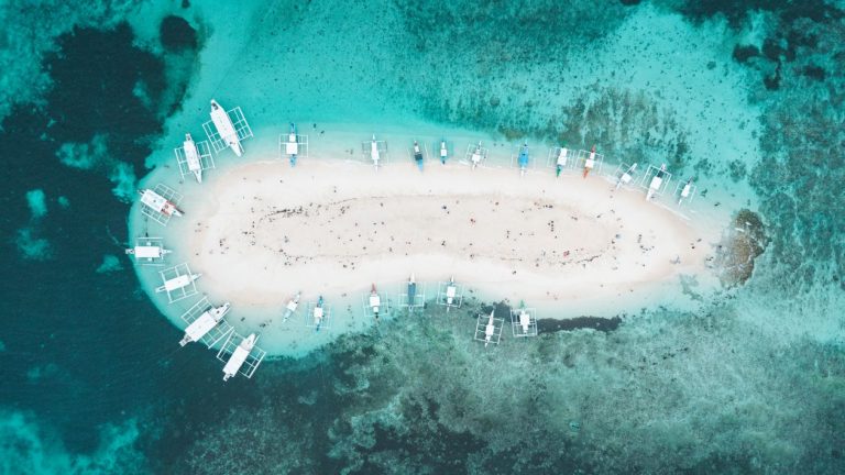 Aerial view of a sandbar with outrigger boats anchored around it, showcasing a popular destination during the best time to visit Philippines when waters are calm and clear.