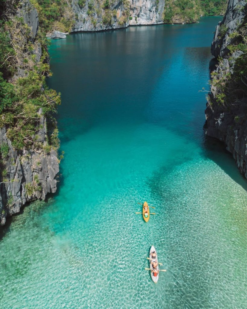 Tourists paddle kayaks through the turquoise waters of Big Lagoon, framed by jagged limestone cliffs—one of the best tours in El Nido for kayaking.