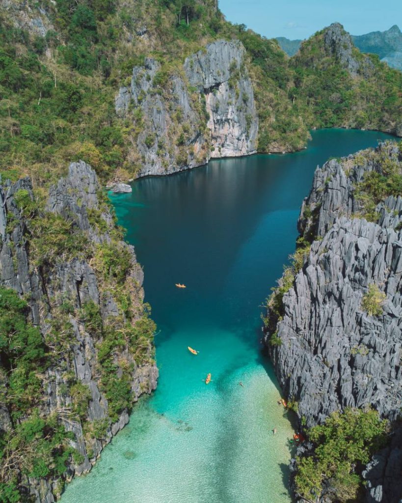 A breathtaking aerial view of Big Lagoon in El Nido, Philippines, featuring towering limestone cliffs, emerald-green waters, and kayakers exploring the lagoon. A great place to see in the Philippines, known for its dramatic scenery and serene waters.