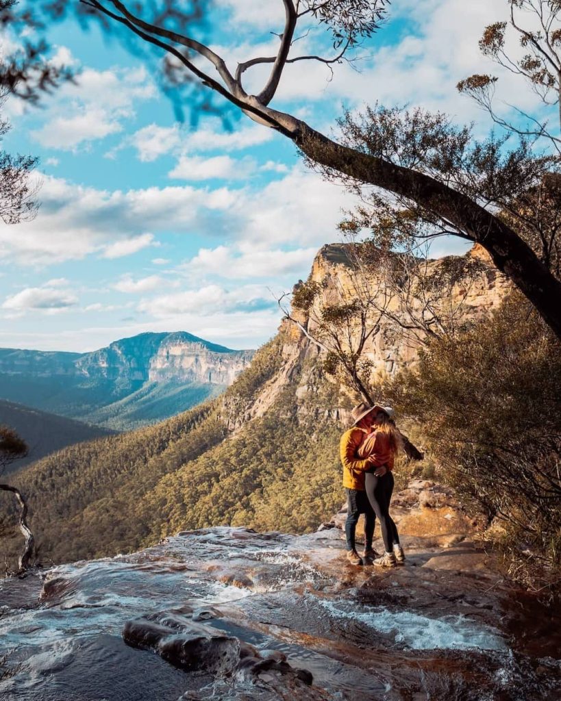A couple embraces at the top of Fortress Falls, surrounded by forested cliffs and cascading water—one of the most romantic things to do in the Blue Mountains.