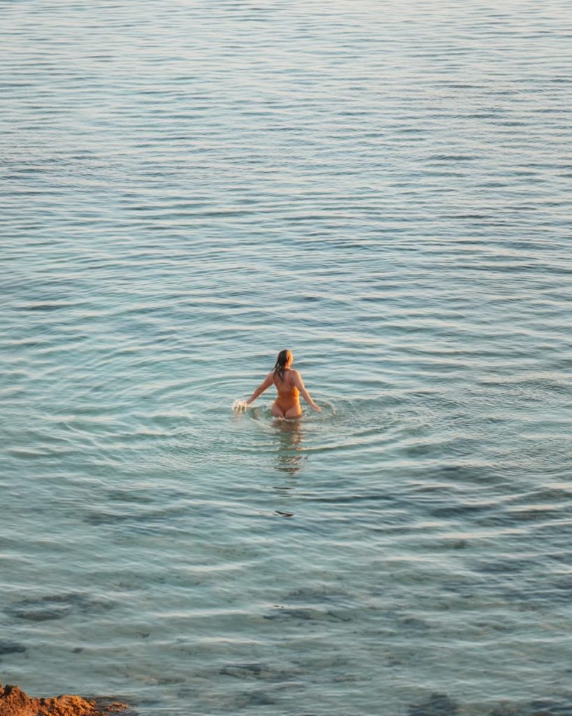 A woman stands in the calm shallows with her arms raised toward the sunset, soaking in the peaceful vibe of one of El Nido’s best tours.