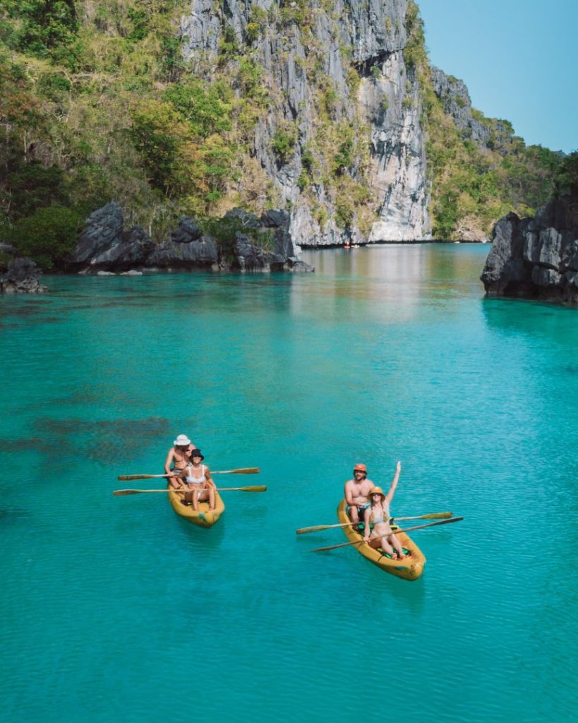 Tourists kayaking through the crystal-clear waters of Big Lagoon, El Nido, surrounded by towering limestone cliffs, highlighting the affordable cost of traveling the Philippines.