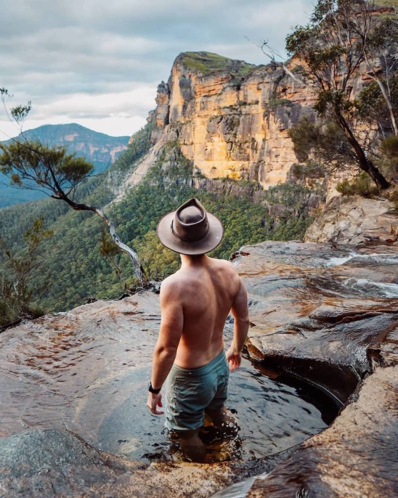 A man stands waist-deep in a natural pool at Fortress Falls, taking in epic views of sandstone cliffs—this hidden spot is among the top things to do in the Blue Mountains.