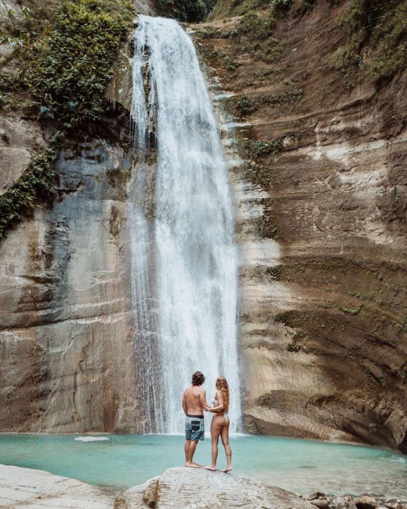 A couple admiring a majestic waterfall in Cebu, Philippines, surrounded by lush greenery, proving that breathtaking sights come at a low cost of traveling the Philippines.