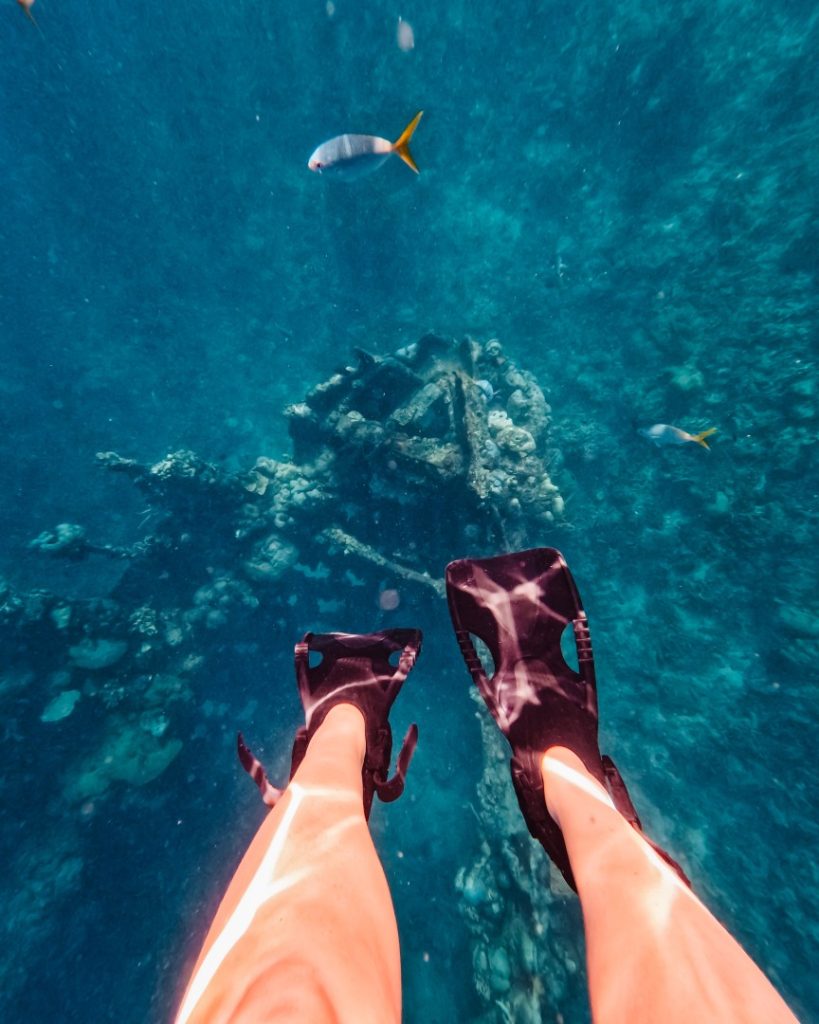 Underwater view of a snorkeler’s legs with fins, floating above the Skeleton Wreck in Coron, where a sunken ship is surrounded by colourful fish. A unique diving spot in the Philippines, perfect for snorkelers and scuba divers.
