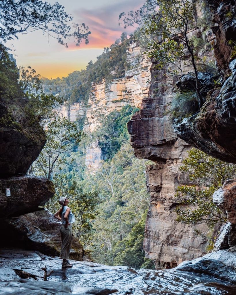 A woman in hiking boots stands at the edge of the infinity pool at Leura Cascades, framed by cliffs and trees—one of the most photogenic things to do in the Blue Mountains.