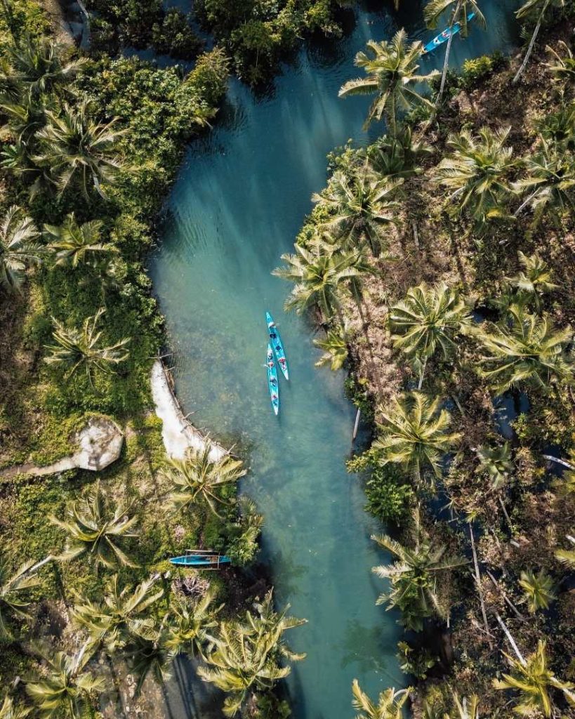 Aerial view of a tropical river in Siargao, Philippines, lined with palm trees and kayaks floating through the water, showing the Philippines travel cost can be low while exploring paradise.