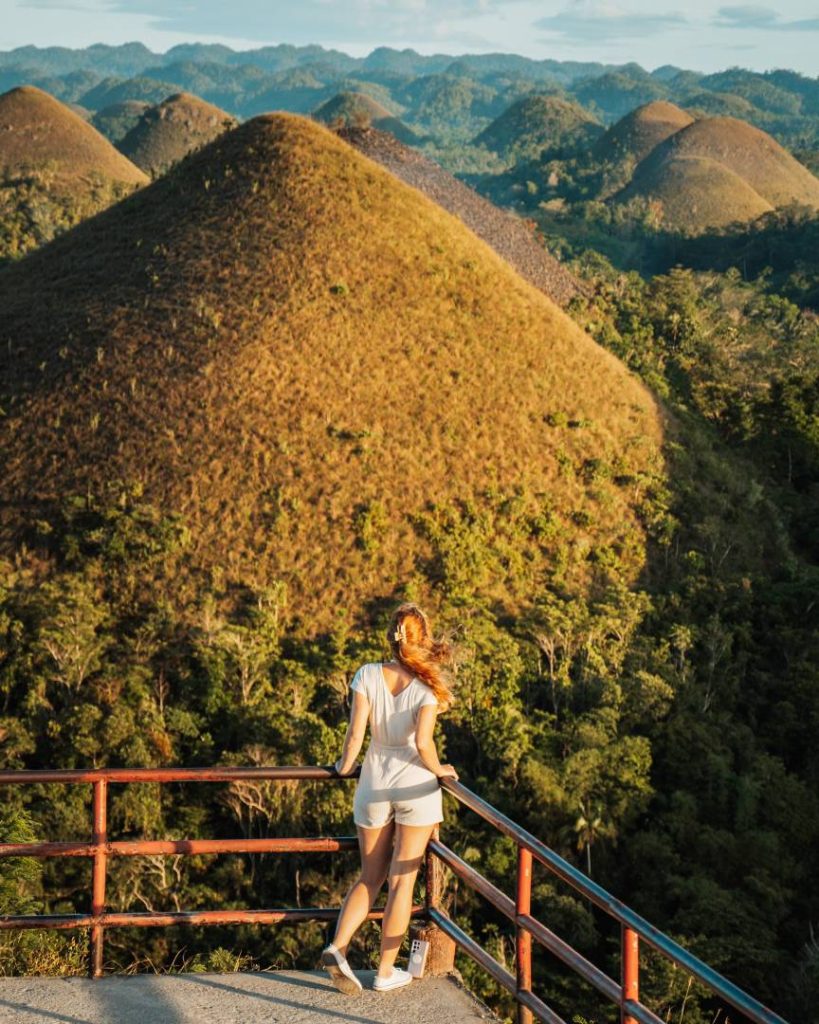 A woman standing at a viewpoint overlooking the Chocolate Hills in Bohol, Philippines, with rolling green hills stretching into the distance, proving that breathtaking nature comes at an affordable Philippines travel cost.