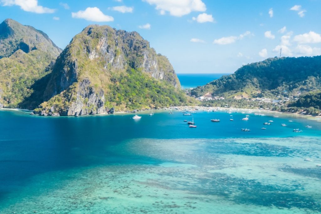 A scenic aerial shot of El Nido, Palawan, showcasing towering limestone cliffs, vibrant blue waters, and scattered boats. One of the best spots to check out in the Philippines, perfect for island hopping and beach adventures.