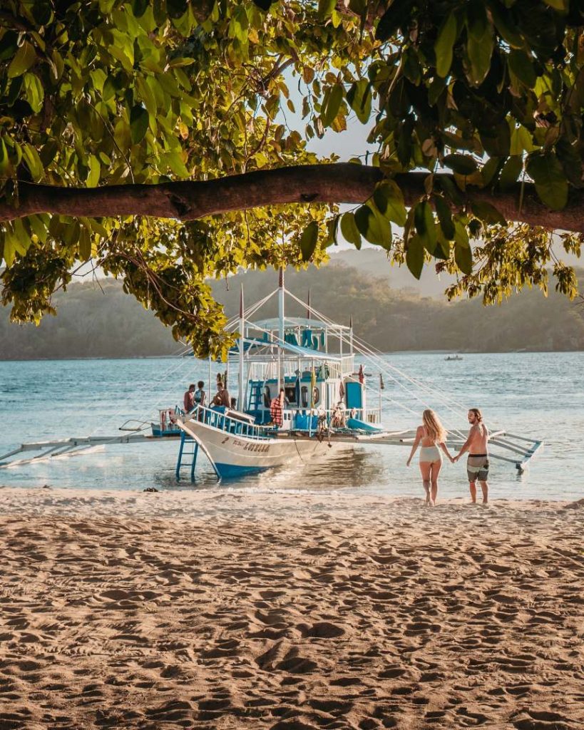 Couple walking towards a traditional Filipino outrigger boat on a beach, getting ready for island hopping during the best time to visit Philippines coastal areas.