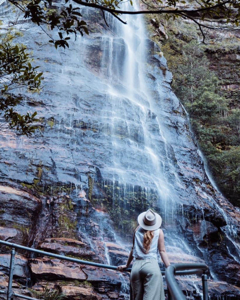 A woman relaxes in a natural infinity pool at Leura Cascades, overlooking a lush valley—an adventurous and scenic thing to do in the Blue Mountains.