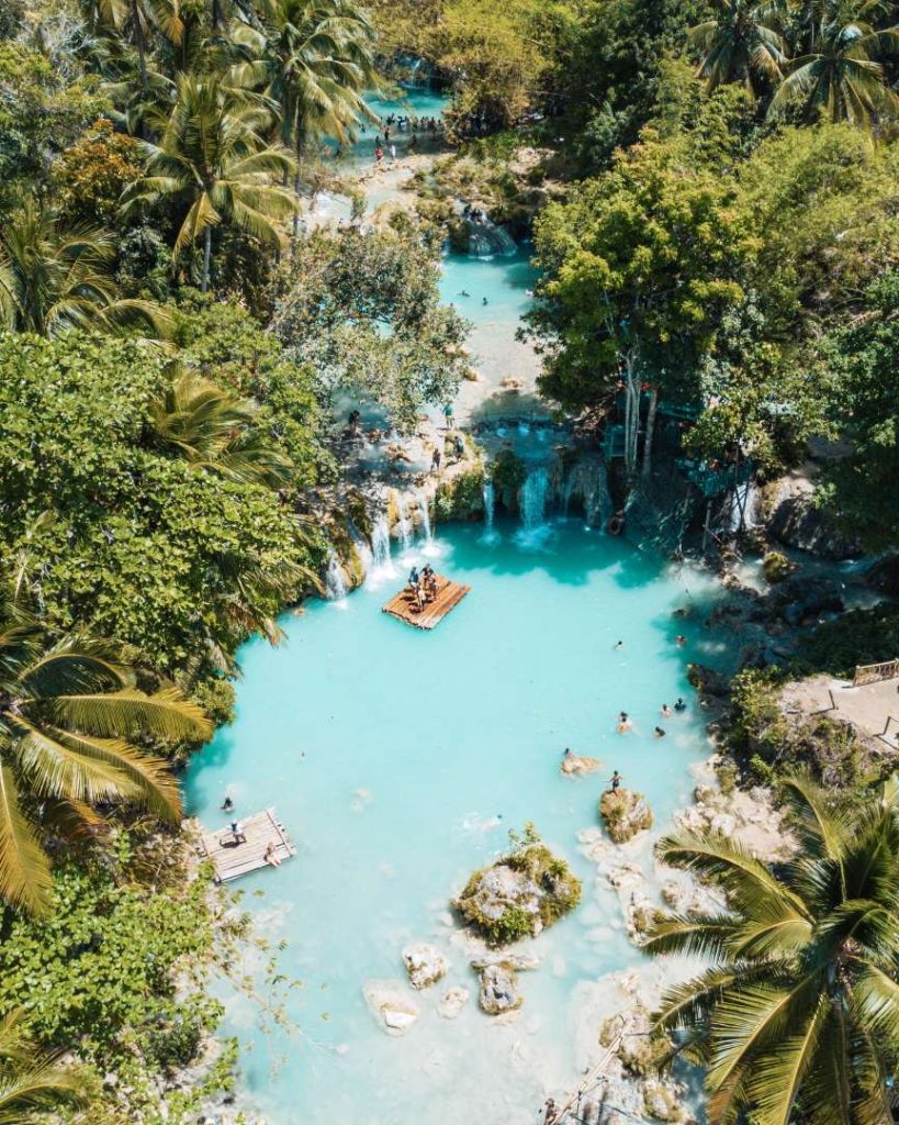 Aerial view of Cambugahay Falls in Siquijor with turquoise pools, palm trees, and bamboo rafts, best enjoyed during dry season in the Philippines.