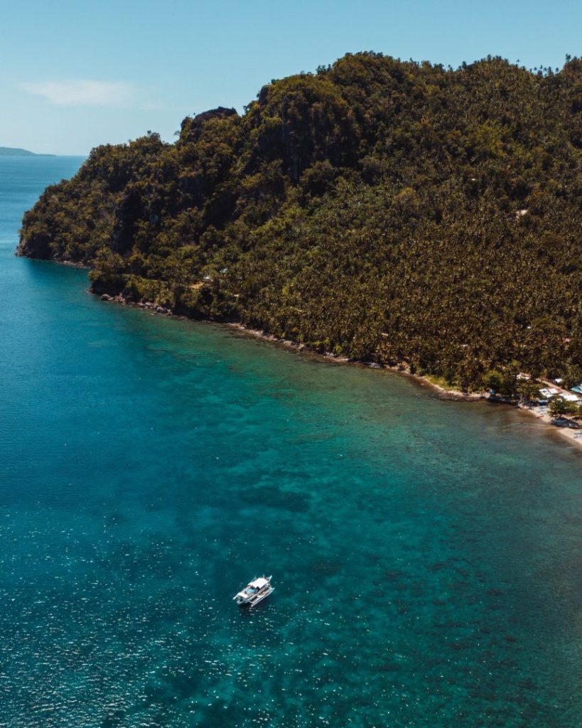 A white boat floats on crystal-clear waters near Pescador Island, surrounded by lush coastline—a relaxing and scenic thing to do in Cebu.