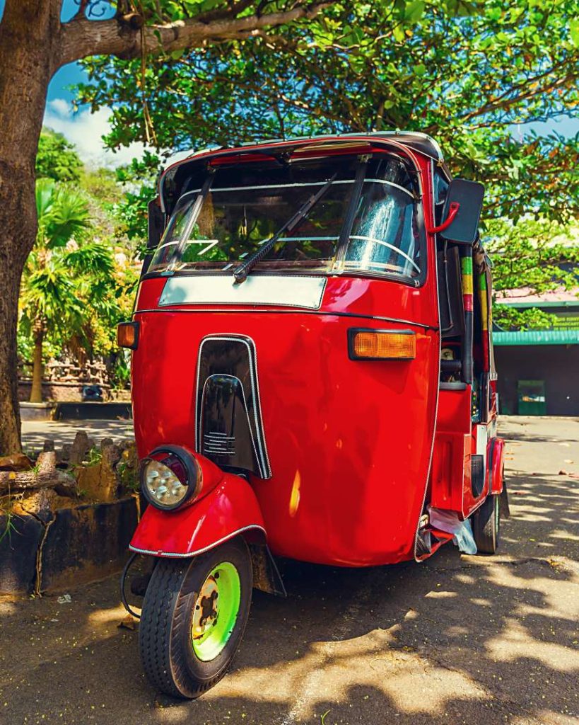 A vibrant red tuk-tuk parked under a tree in a tropical setting, with greenery in the background, emphasizing how local transport keeps the cost of traveling the Philippines budget-friendly.