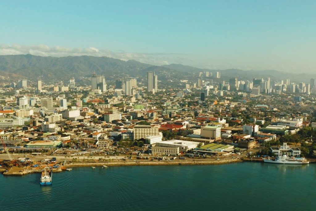 Aerial view of Cebu City, showing high-rise buildings, mountains in the background, and the waterfront—urban exploration is another side of things to do in Cebu.