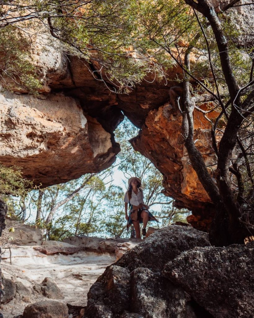 A woman stands before the base of Wentworth Falls, watching the water stream down a rugged cliff—hiking here is a top activity in the Blue Mountains.