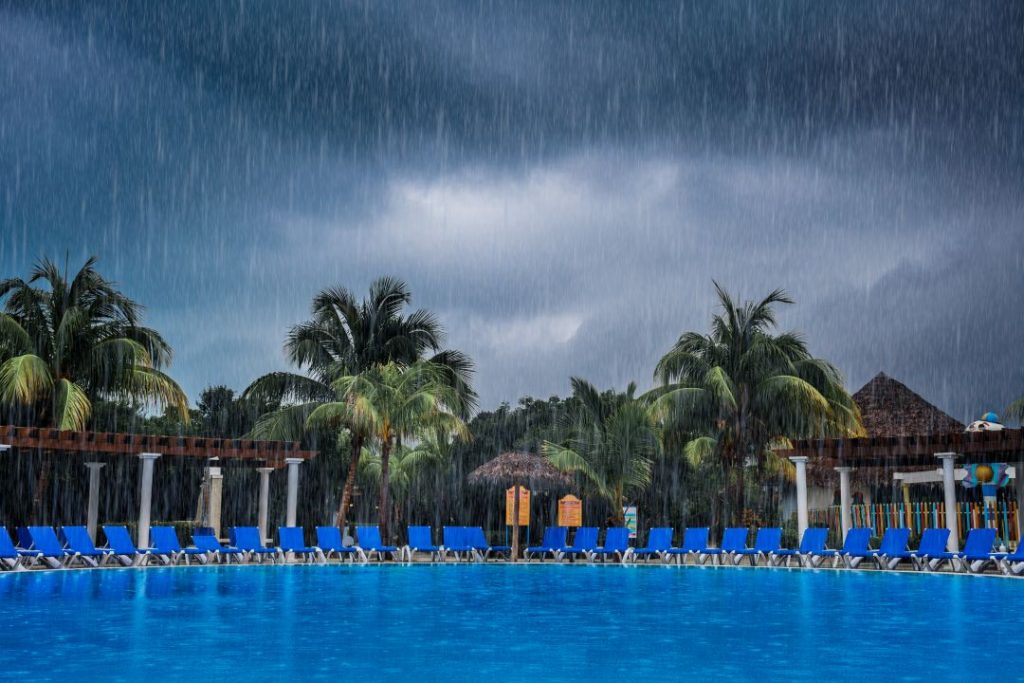 Tropical resort pool with empty blue chairs under heavy rain, showing the wet season in the Philippines and why timing your visit matters.
