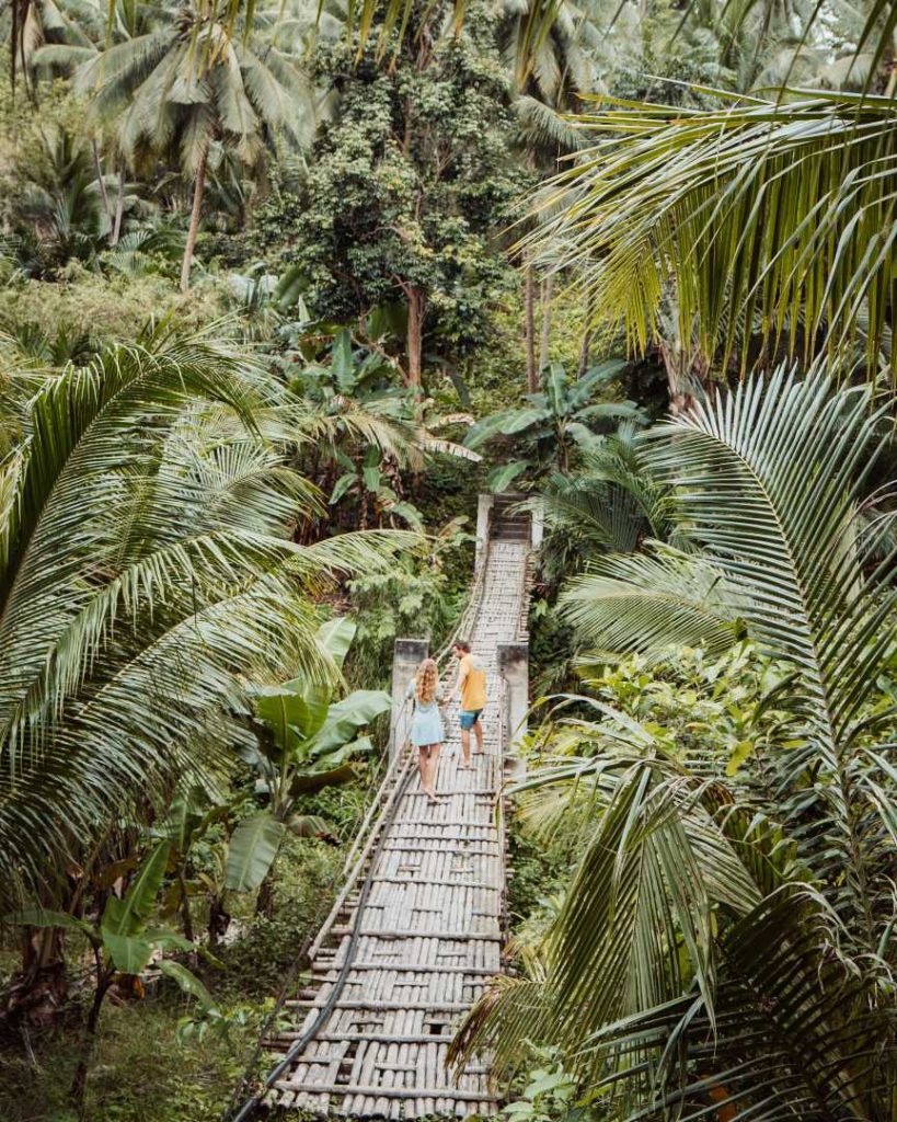 A couple walks across a bamboo suspension bridge surrounded by dense jungle—hiking to Cebu’s hidden waterfalls is one of the best nature-filled things to do in Cebu.